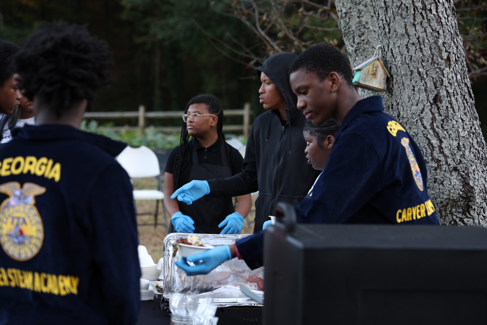 FFA students in blue jackets serving food under the big tree at last fall's festival