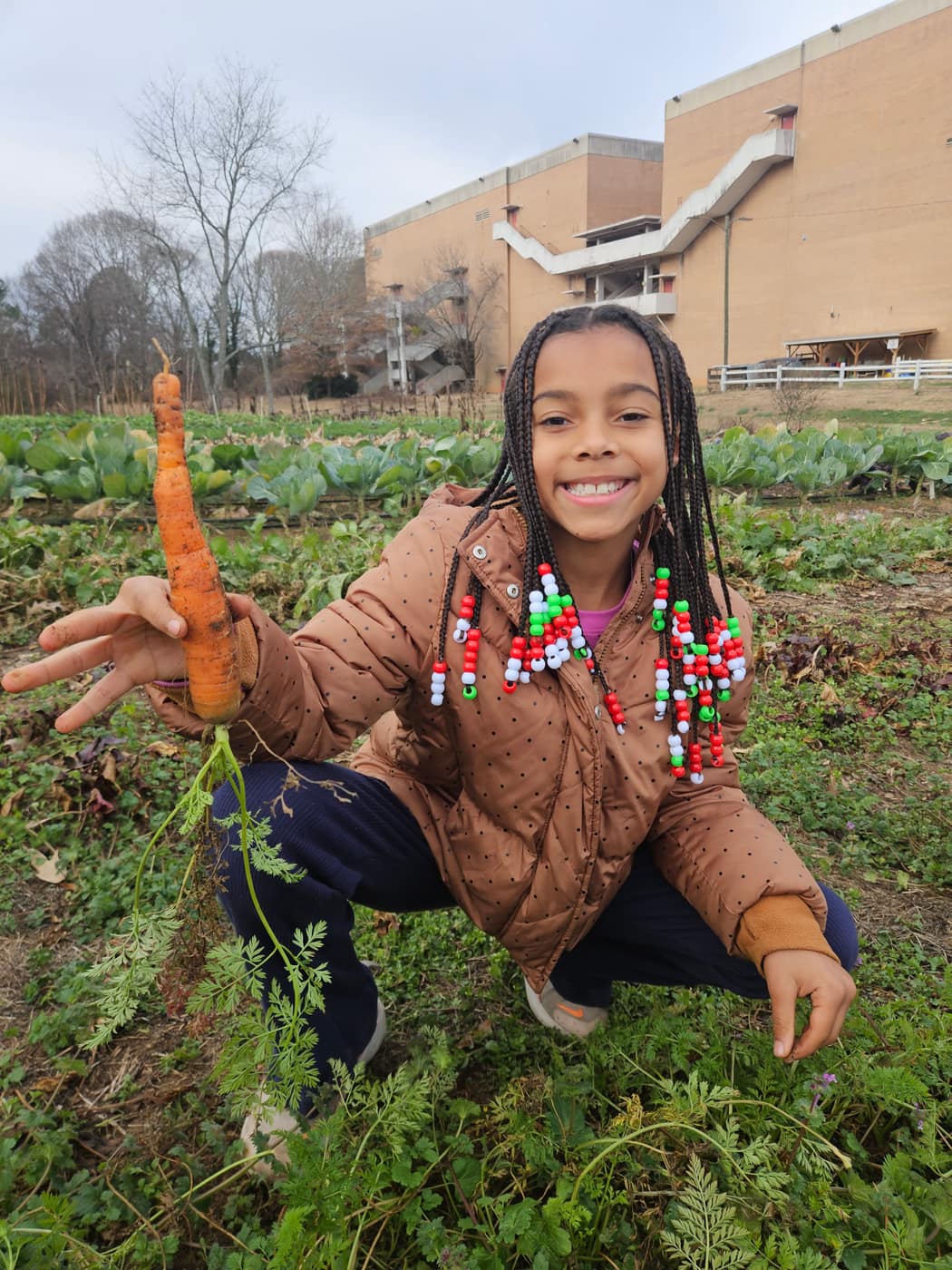 A girl crouched in the field holding up a fresh carrot