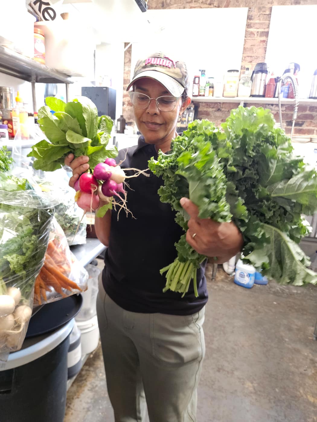 Rahel Tafari in the Grant Park Coffeehouse kitchen holding bunches of radishes and kale from the farm